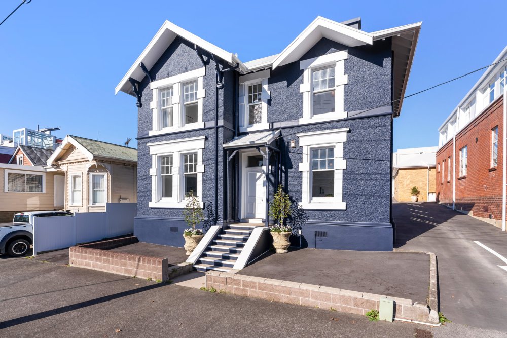 Two-storey heritage building, Sergeants House, with dark blue roughcast exterior, white sash windows, and a central entrance with steps and potted plants