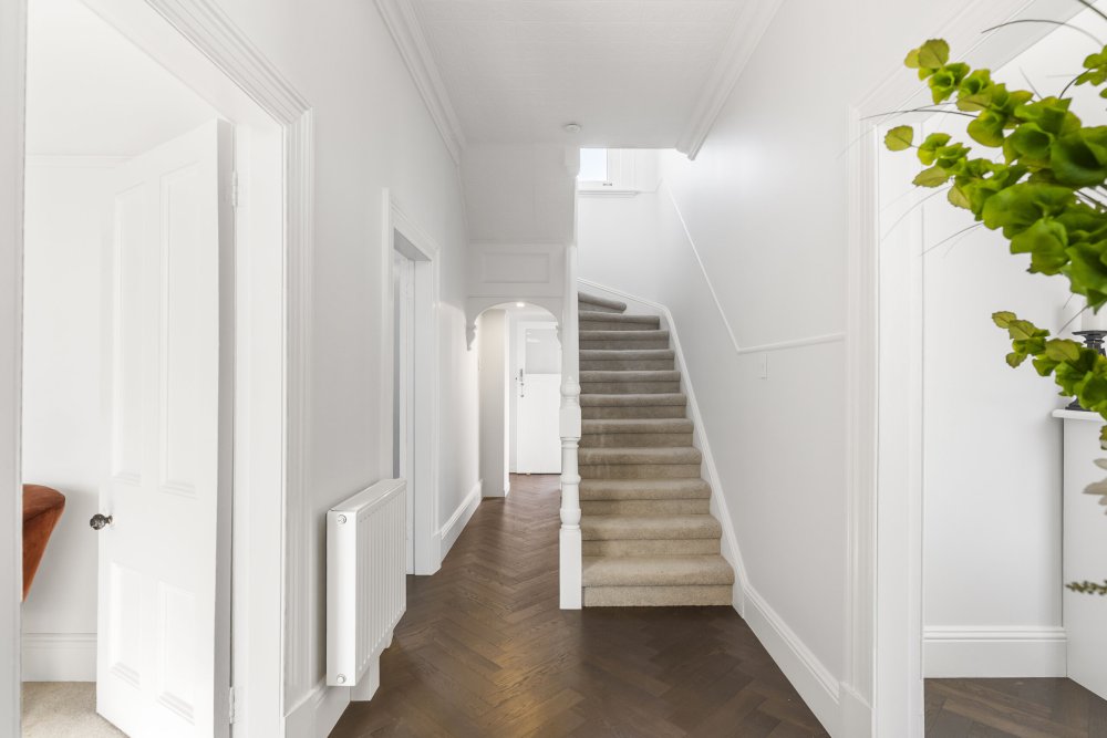 Hallway with dark herringbone timber floors, carpeted staircase, white walls with ornate cornicing, and a radiator