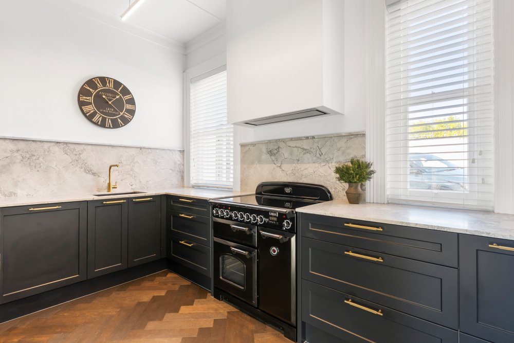 Classic kitchen with dark cabinetry, gold handles, marble splashback, black range cooker, and herringbone timber flooring